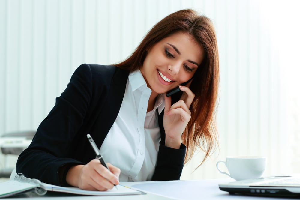 Young happy businesswoman talking on the phone and writing notes in office Young happy businesswoman talking on the phone and writing notes in office